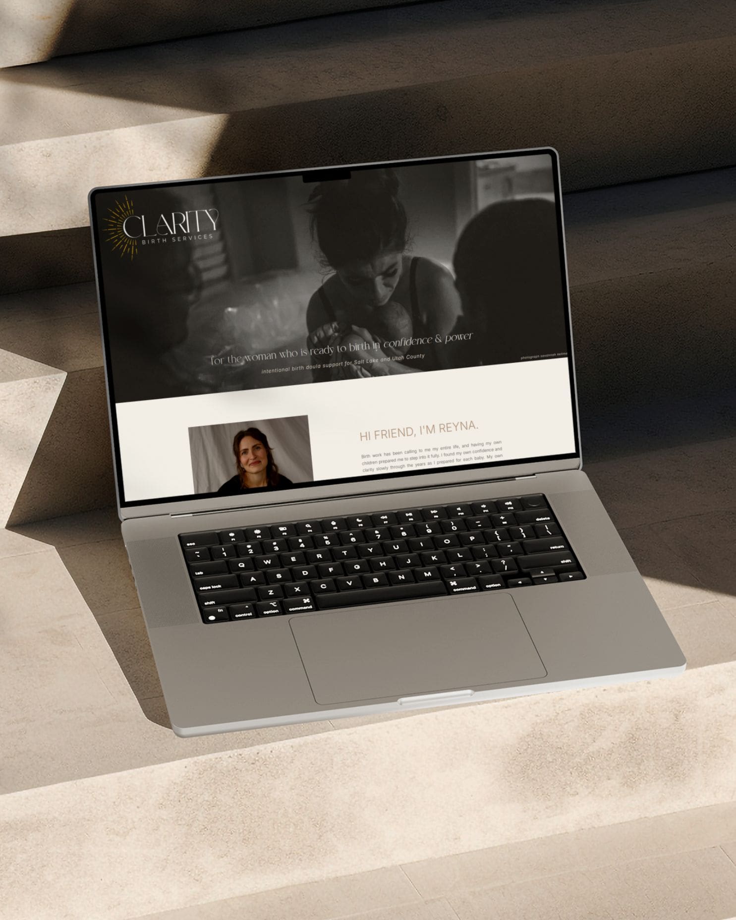 Laptop on sunlit stone steps showing the homepage of the Clarity Birth Services doula website, a custom Showit site designed by Her Brand Designs.